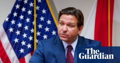 Governador Ron DeSantis em evento oficial com bandeiras dos EUA e Flórida