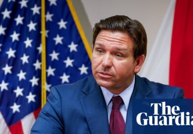 Governador Ron DeSantis em evento oficial com bandeiras dos EUA e Flórida