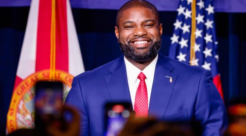 Byron Donalds em evento político em Miami com bandeiras da Flórida e dos EUA