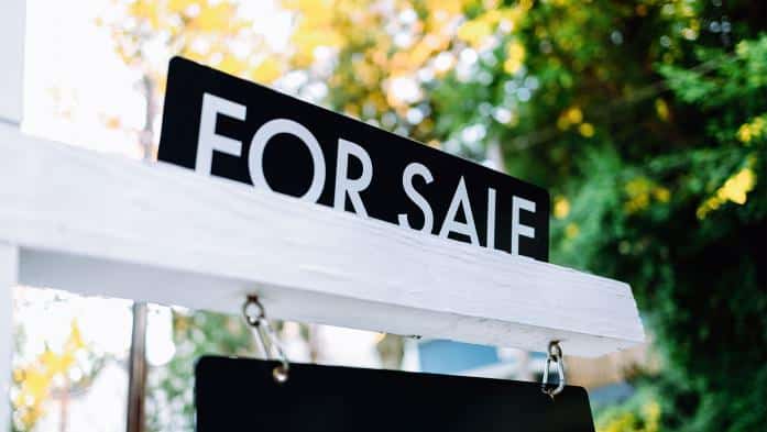 Placa de For Sale (vende-se) em frente a uma casa